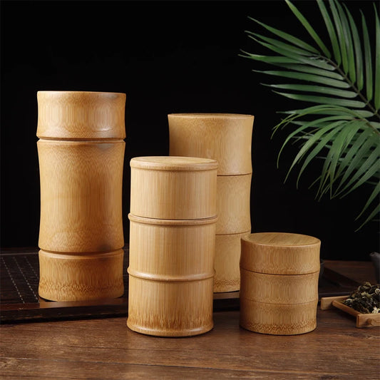 Set of bamboo containers on a wooden surface with a dark background and green leaves.