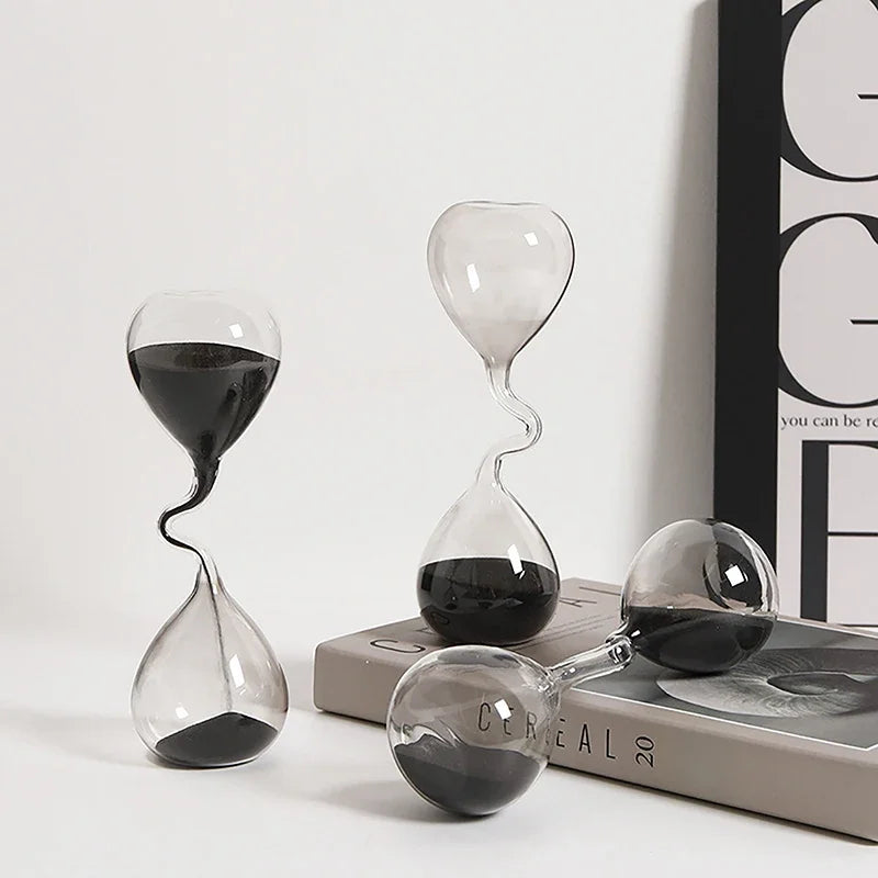 Three glass hourglasses with sand running through them on a white surface.