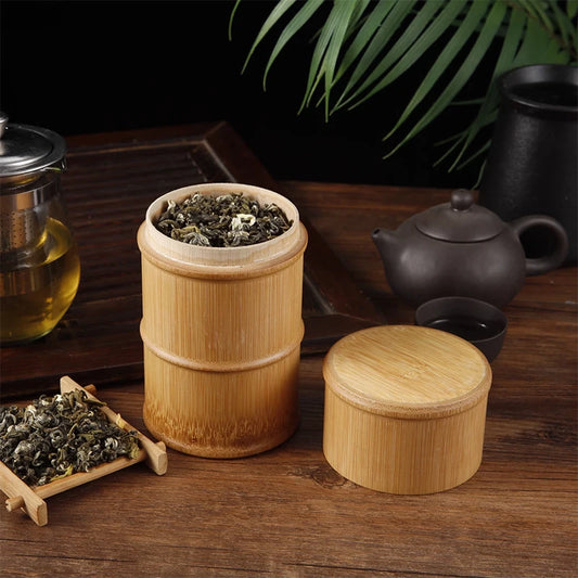 Bamboo container with tea leaves on a wooden surface with tea-making items.