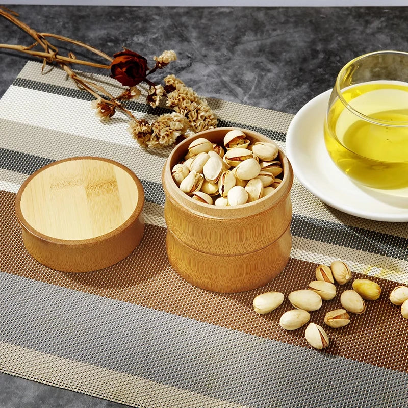Wooden container with pistachios on a table with a cup of tea and dried flowers.