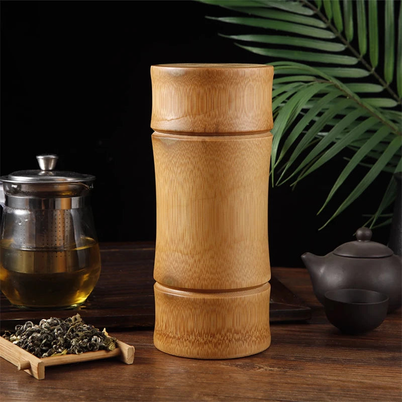 Bamboo tea grinder on a wooden table with tea-making items and leaves in the background