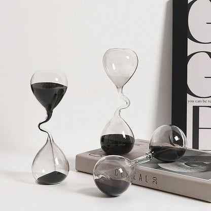 Three glass hourglasses with sand running through them on a white surface.