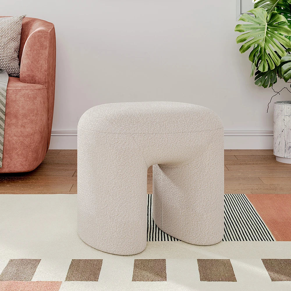 Beige textured stool in a living room setting with a pink armchair and plant.