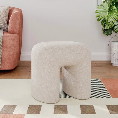 Beige textured stool in a living room setting with a pink armchair and plant.