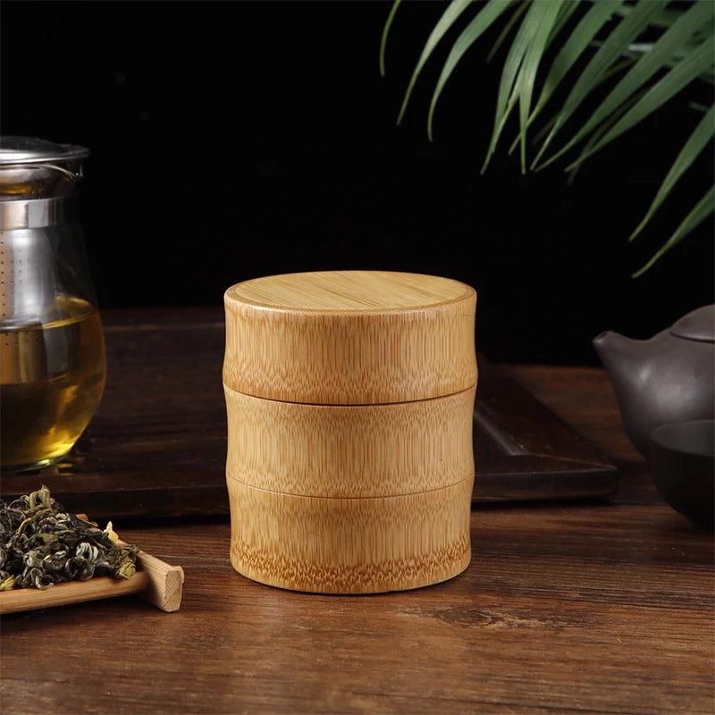 Bamboo tea container on a wooden surface with tea leaves and a teapot in the background.