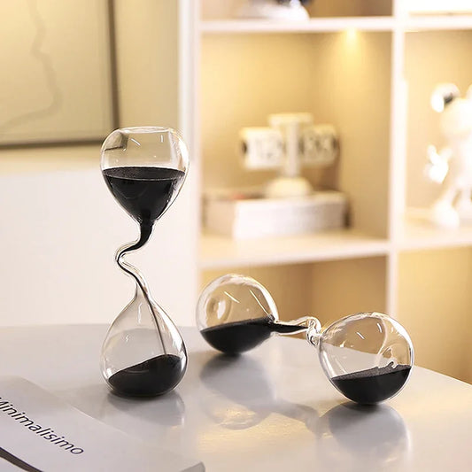 Two glass hourglasses with sand running down on a surface with a blurred background