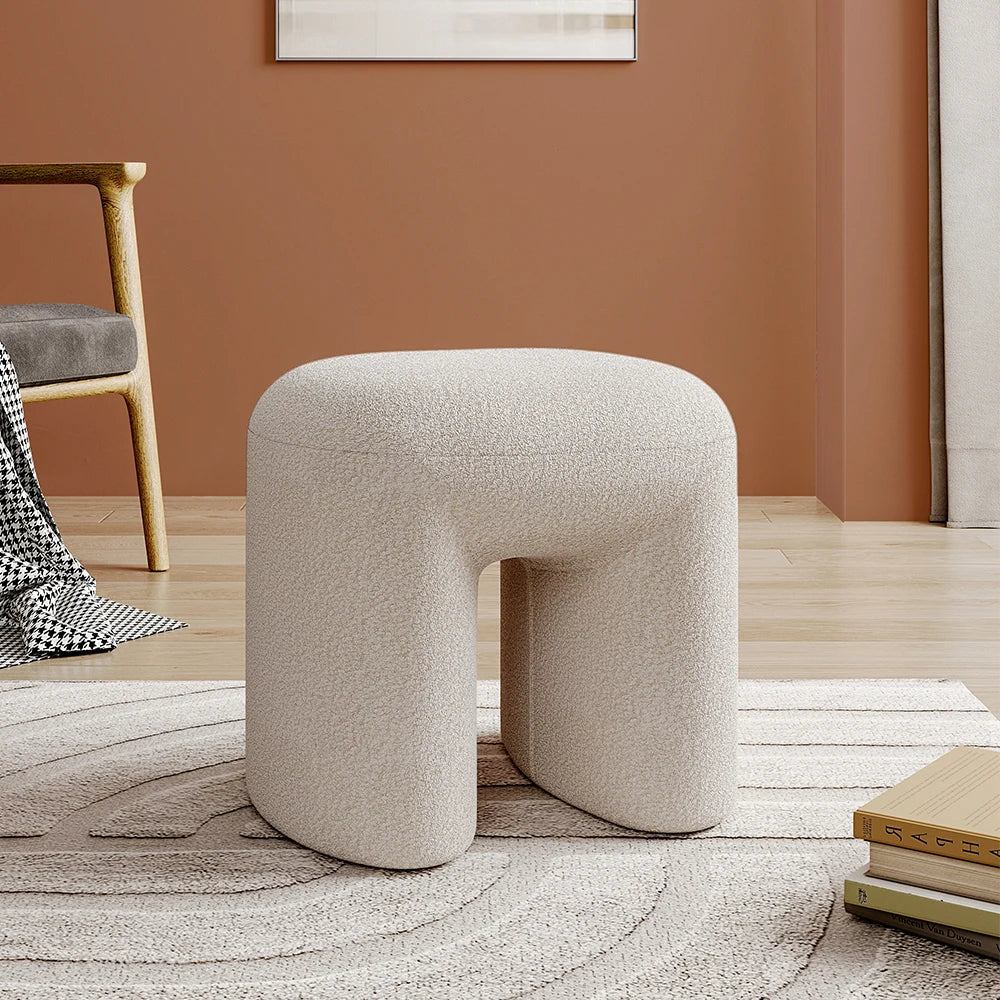 Beige textured stool in a room with a chair and books on a rug.